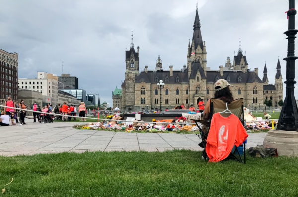 woman waited for the march to start. She looked onto the Centennial Flame around which people left children’s shoes and toys—objects that memorialize the Indigenous children who were forced into residential schools.