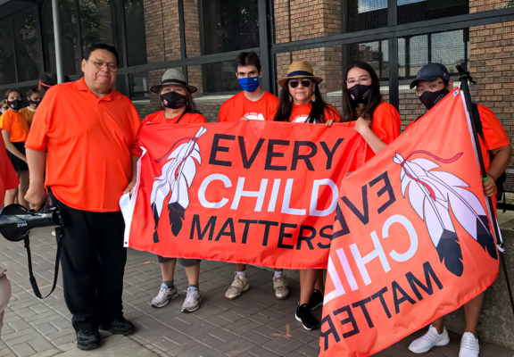 Group stands with a banner on which every child matter is written