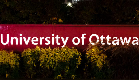 A sign titled ‘University of Ottawa’ slightly placed behind a bush.