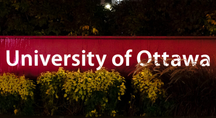 A sign titled ‘University of Ottawa’ slightly placed behind a bush.