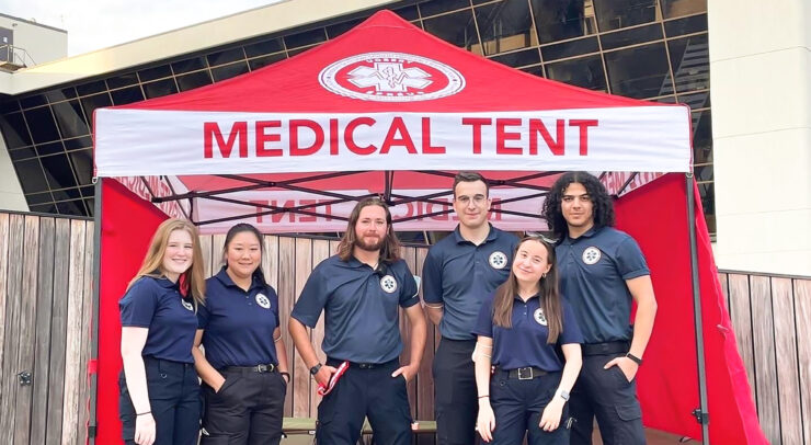 Photo of five team members of VCRT wearing blue uniforms and standing in front of red medical tent