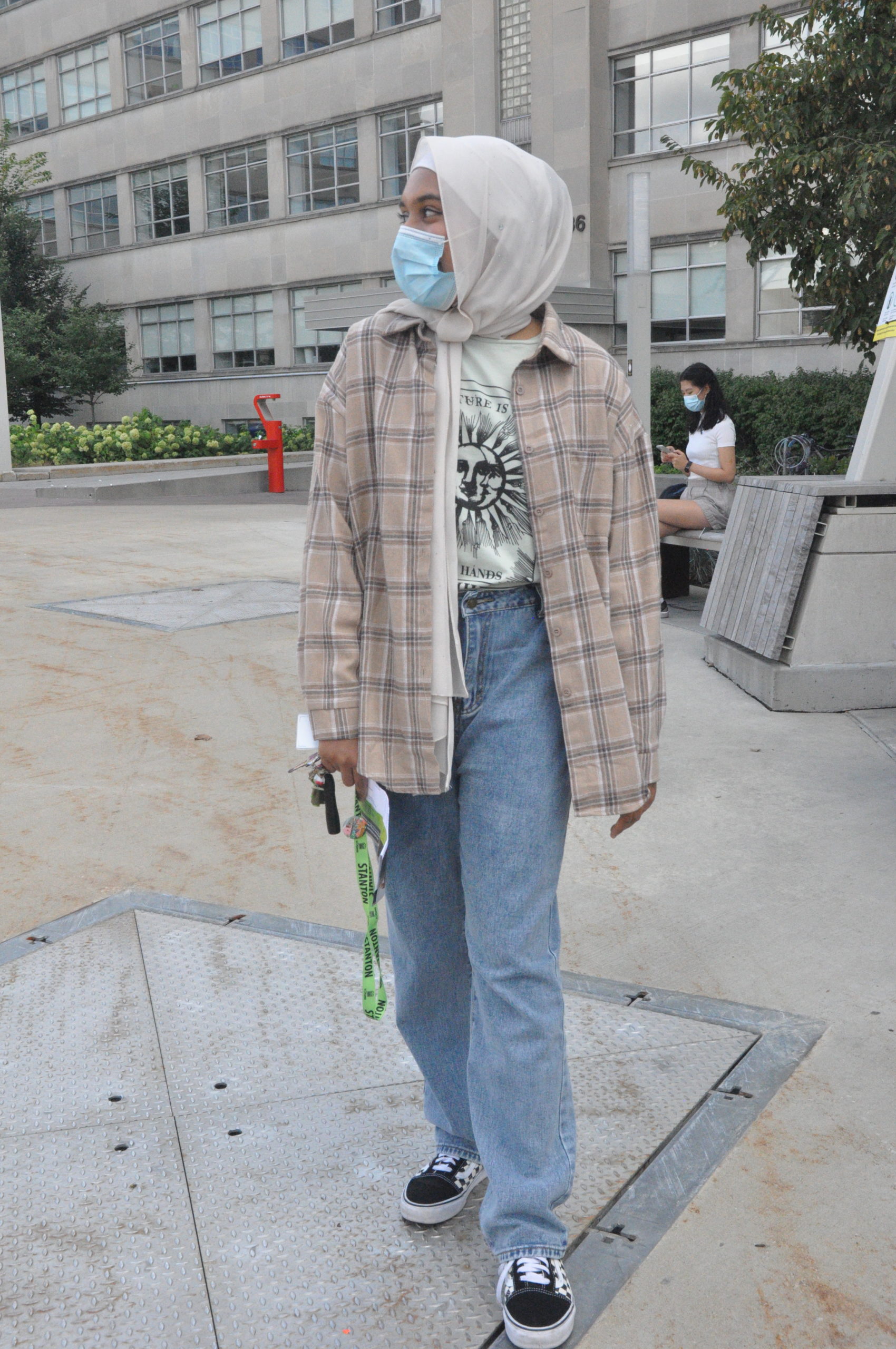 Student posing on campus wearing a beige flannel and light blue jeans