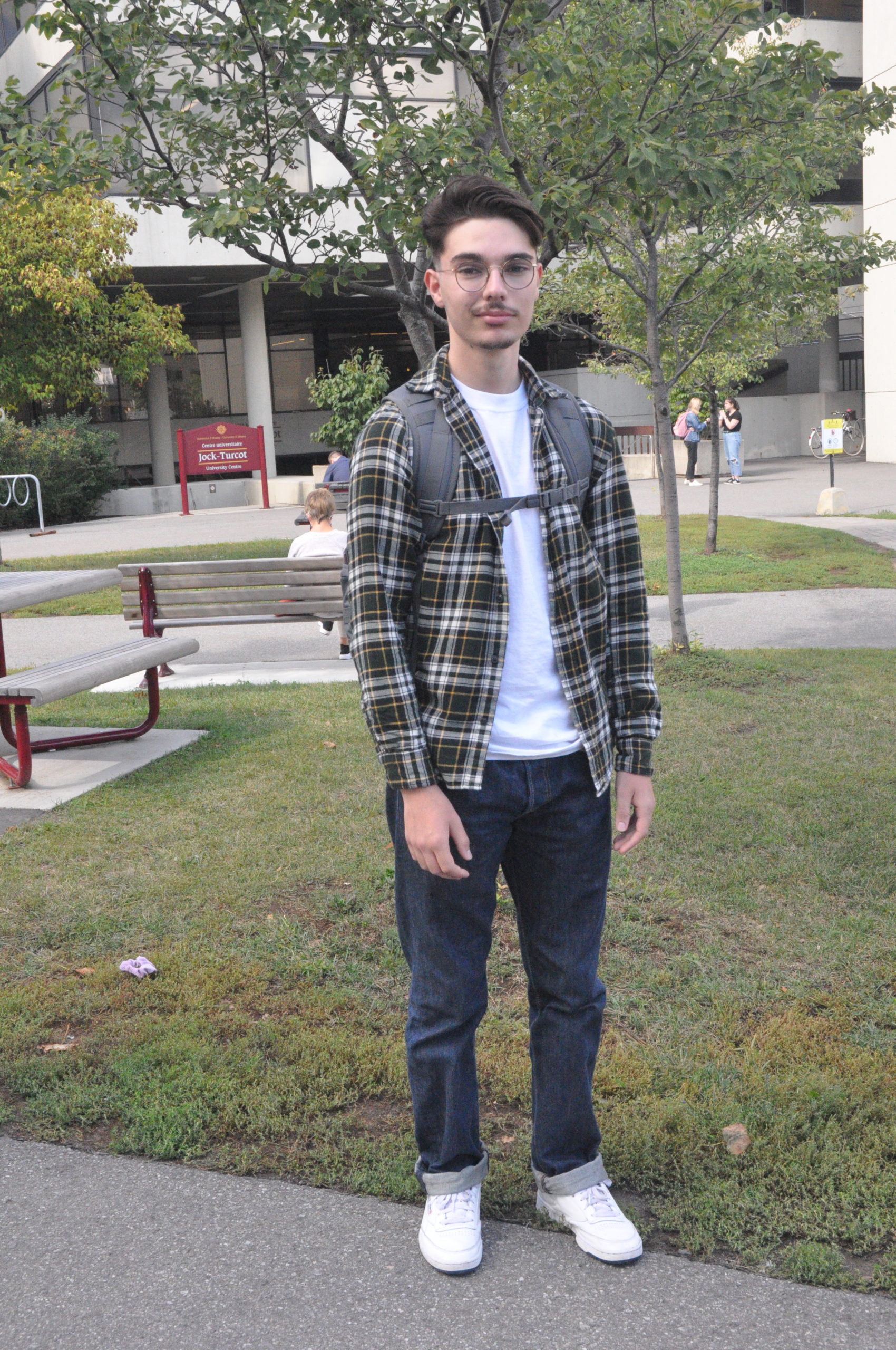 Student posing on campus wearing a green flannel and dark blue jeans