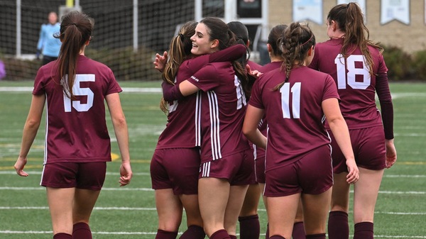 A group of women's soccer players walking away from the camera. Two players are hugging.