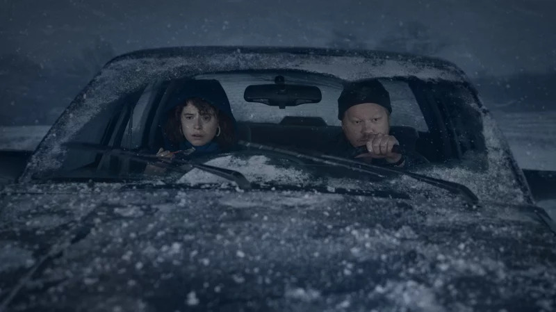 A romantic couple sitting in a snow covered car, looking awkward.