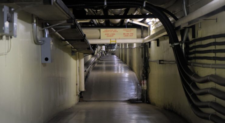 A long, significantly steep hallway which acts as a tunnel under the university. There are pipes along the side wall and on the ceiling.