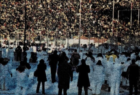 A blurry picture of the crowd surrounding the ice surface, showing volunteers dressed in snow suits