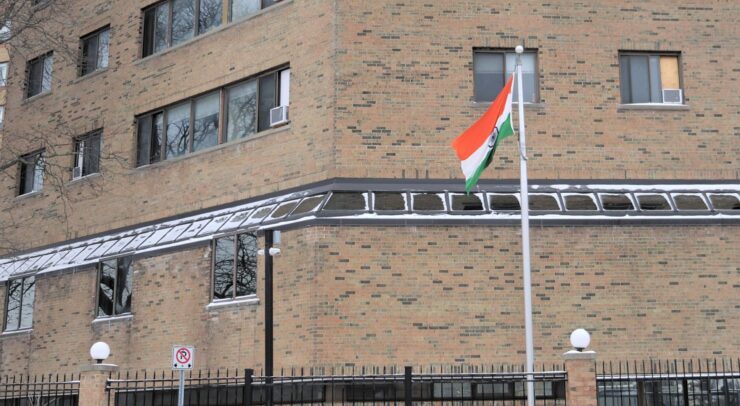 An Indian flag on a flagpole stands outside an angled tall brick building