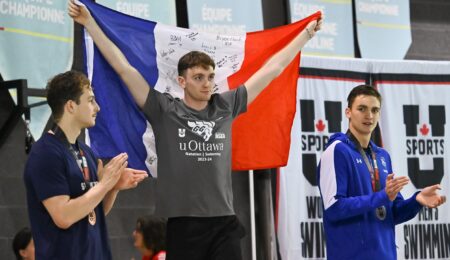 A young man holds up a French flag with signatures in between two other men, who are clapping