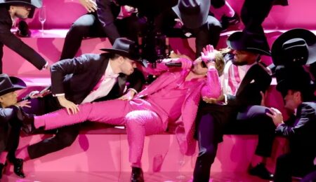 Ryan Gosling in a pink sparkling suit leans against back-up dancers