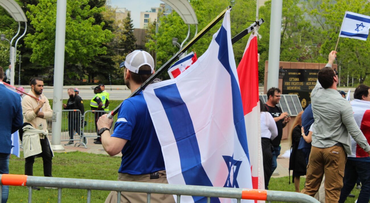 man holding israel and canadian flags on hockey sticks