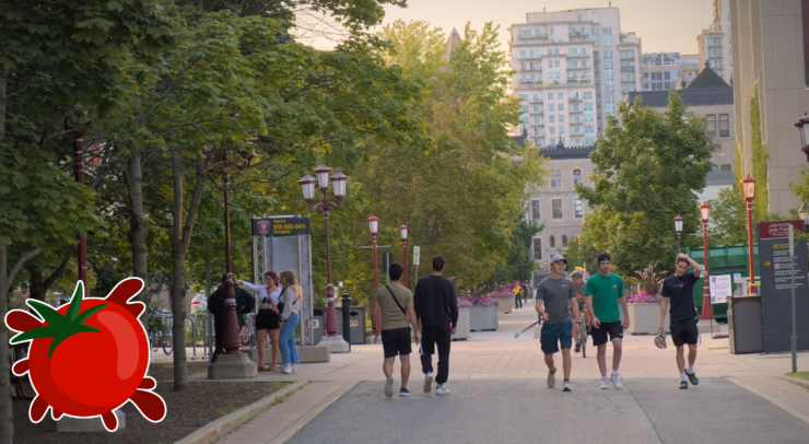 A photo of people walking across a university campus with a tomato logo in the corner