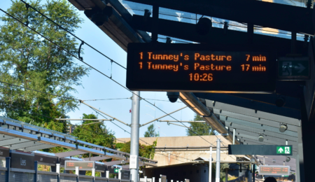 A sign with light rail wait times: “tunney’s pasture comes in 7 mins; tunney’s pasture comes in 17 mins”