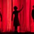 A photo by Kyle Head, a red curtain with three silhouettes.