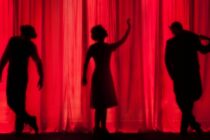 A photo by Kyle Head, a red curtain with three silhouettes.