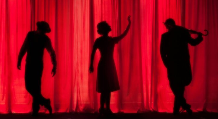 A photo by Kyle Head, a red curtain with three silhouettes.