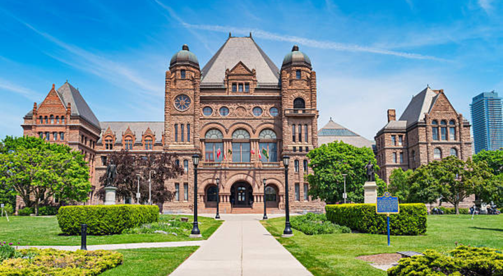 Photo of the facade of the landmark Ontario Legislative Building at Queen's Park in Toronto, Ontario, Canada on a blue sky day. The Ontario Legislative Building is a public building which houses the Legislative Assembly of the province of Ontario.